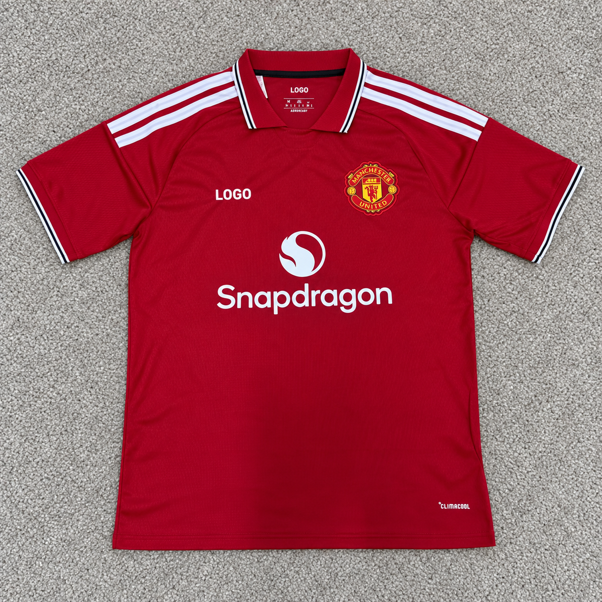 Manchester United · Local 26/27 · Fan · Escudo conservado y LOGO · Alfombra gris